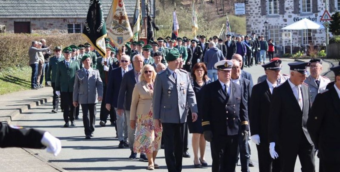 Das Foto zeigt den Festumzug zum Ehrenmal in Sundern-Hellefeld. Neben den Schützen, Reservisten und anderen, lokalen Vereinen mit jeweiligem Banner erkennt man in der Bildmitte auch den Kreisvorsitzenden des Volksbundes im Hochsauerland, Hubert Kleff, sowie den Bezirksvorsitzenden, Regierungspräsident Heinrich Böckelühr.